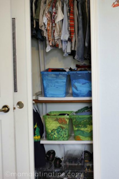 The interior of a closet with kids clothes in the top part and with blue and green boxes with more clothes.