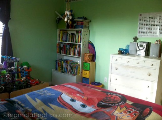 A boys room with green walls, a bookcase, dresser and a bed with lighting McQueen bedspread. 