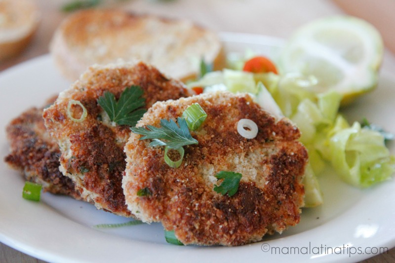 Tuna cakes with parsley leaves and green onion pieces on top, next to a green salad on a white plate