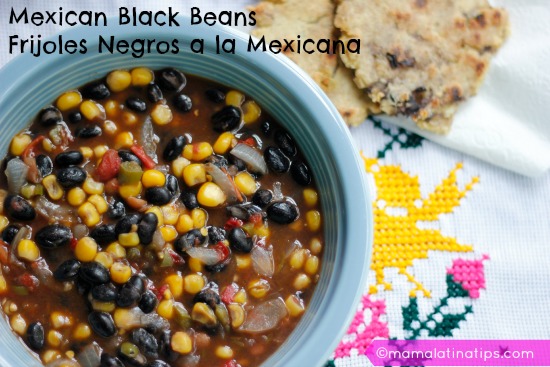 Mexican black beans with corn, onion and tomatoes on a blue bowl. There are two tortillas on the side. 