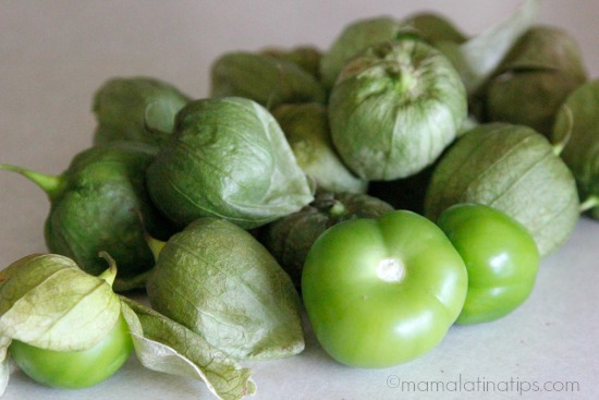 A bunch of tomatillos on top of a white surface. Some tomatillos are peeled, some are not. 