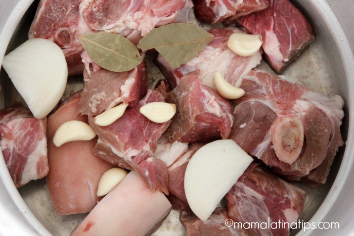 Pork meat in pieces with several cloves of garlic, white onion and bay leaves in a large pot.