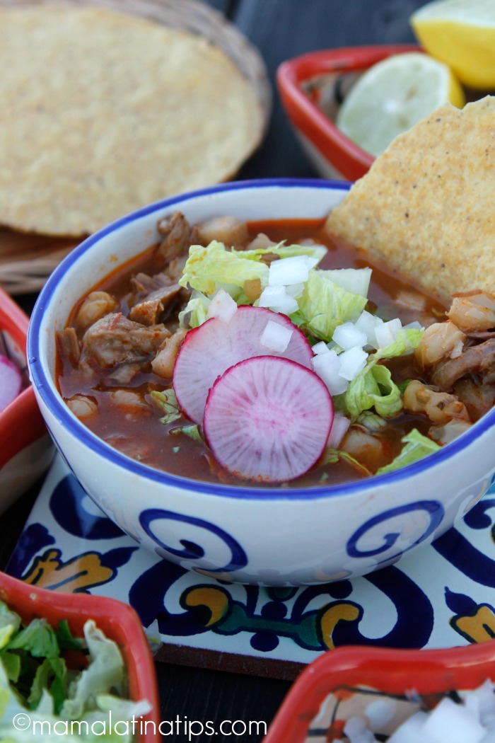 A Mexican bowl with red pozole with pork and topped with lettuce, onions and radishes. 