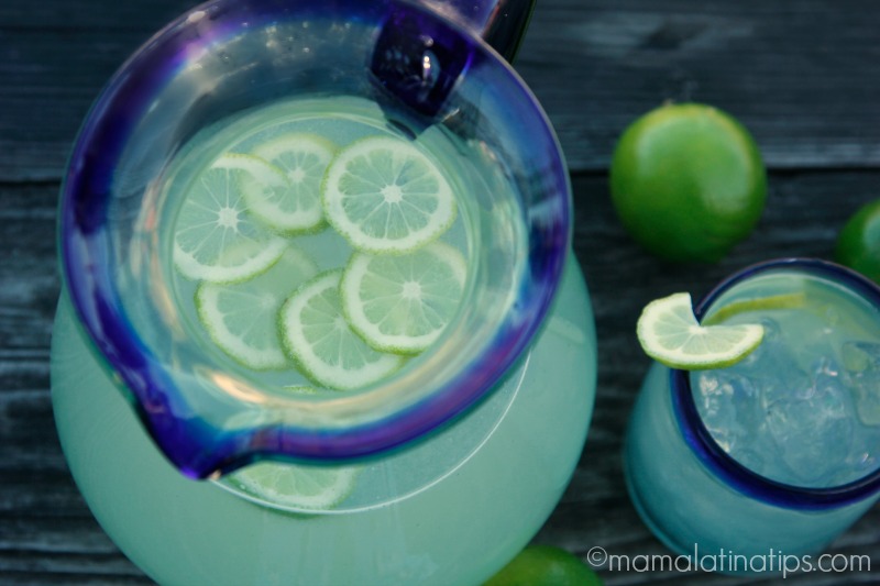 Lime Agua Fresca in a Mexican jar and glass on top of a wooden surface
