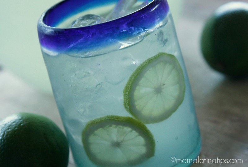 A Mexican glass with blue rim with lime agua fresca and lime slices inside.