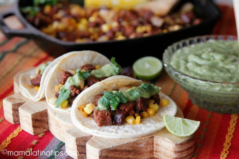 tacos de chorizo con elote desgranado junto a un plato con salsa y limones partidos por mitad