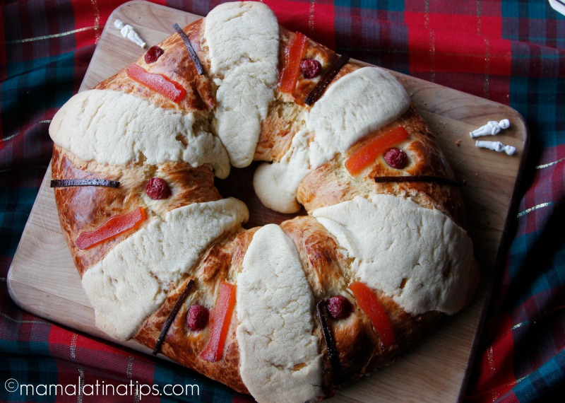 Rosca de reyes con seis costrones y adornada con cerezas y frutas secas sobre una tabla de madera. 