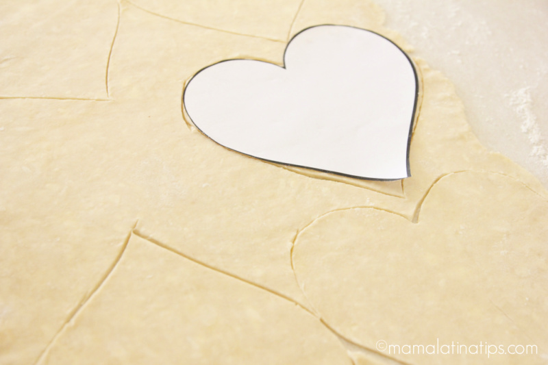Un stencil en forma de corazón sobre una masa de hojaldre extendida y cortada con más corazones.