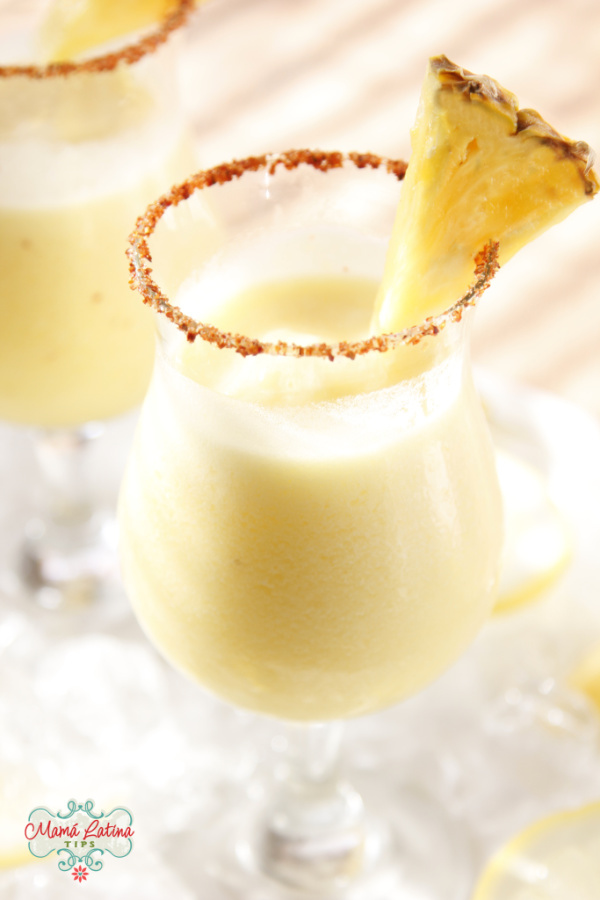 frozen pineapple margarita in a tall glass with a piece of pineapple in the glass rim.