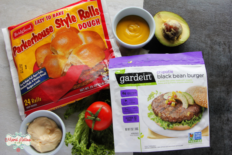 A bag of Parkerhouse style rolls dough, a bag of Chipotle black bean burger patties by gardein, avocado, tomato, lettuce and condiments.