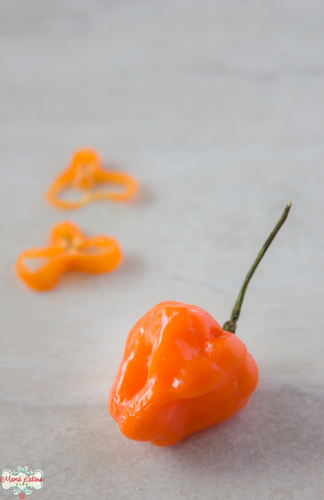 Un chile habanero y varias rodajas de chile sobre una mesa blanca. 