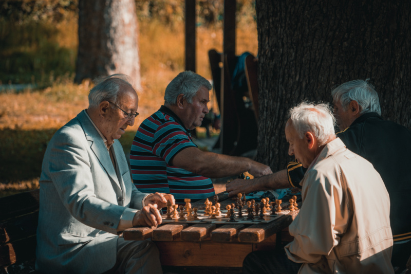 senior citizens playing chess in a wooden table outdoors