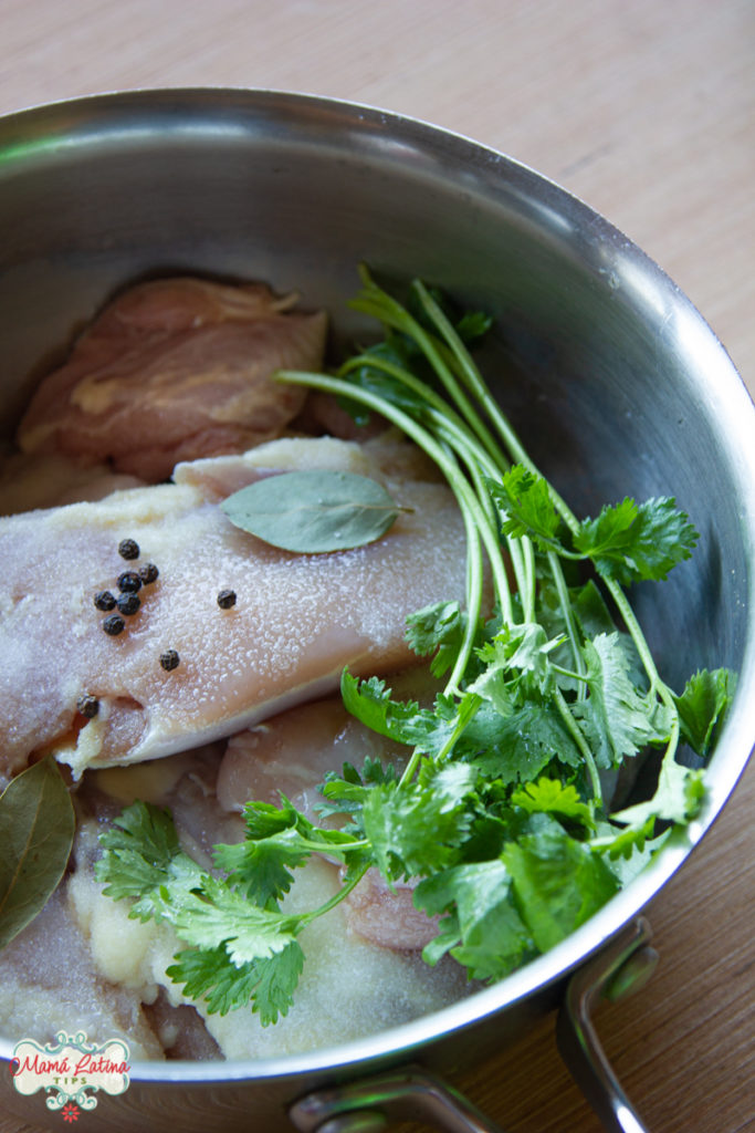 Carne de pollo cruda en una olla con cilantro, pimienta y laurel