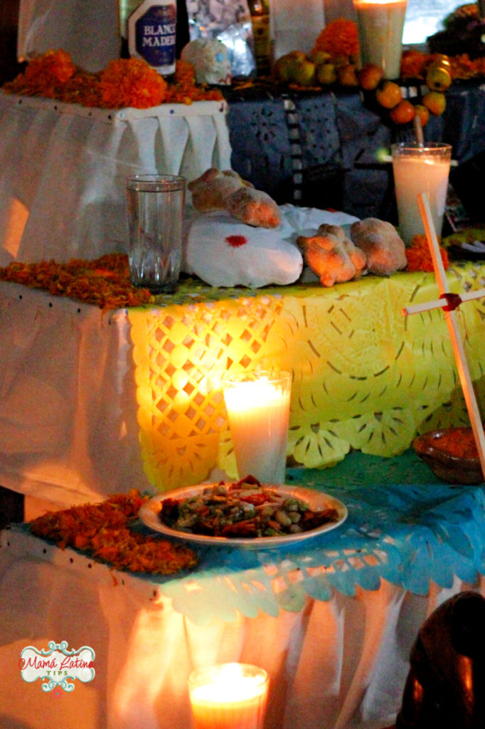 A glass of water, pan de muerto, candles and papel picado on a Day of the Dead Altar
