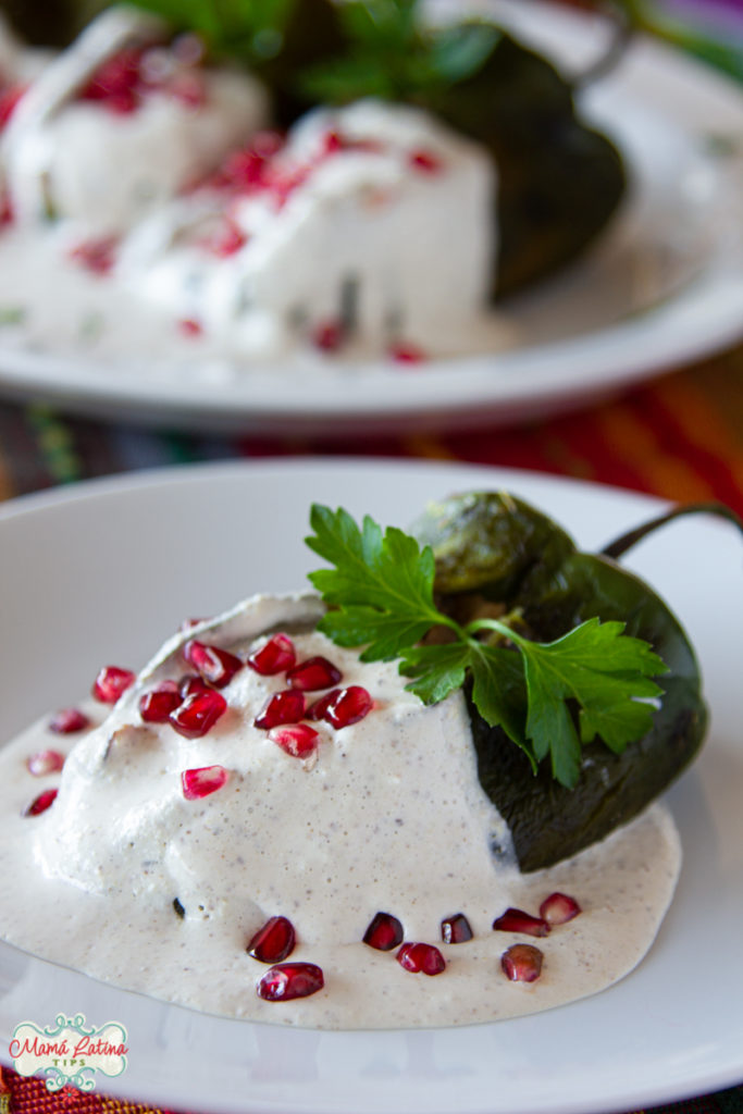 Un chile en nogada sobre salsa blanca de nuez de castilla, adornado con granos de granada y hojas de perejil.