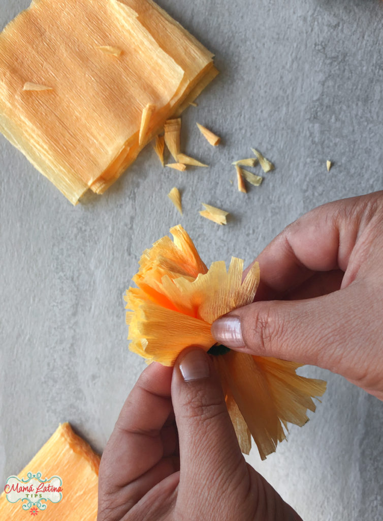 A person separating layers of crepe paper to make a paper marigold flower.