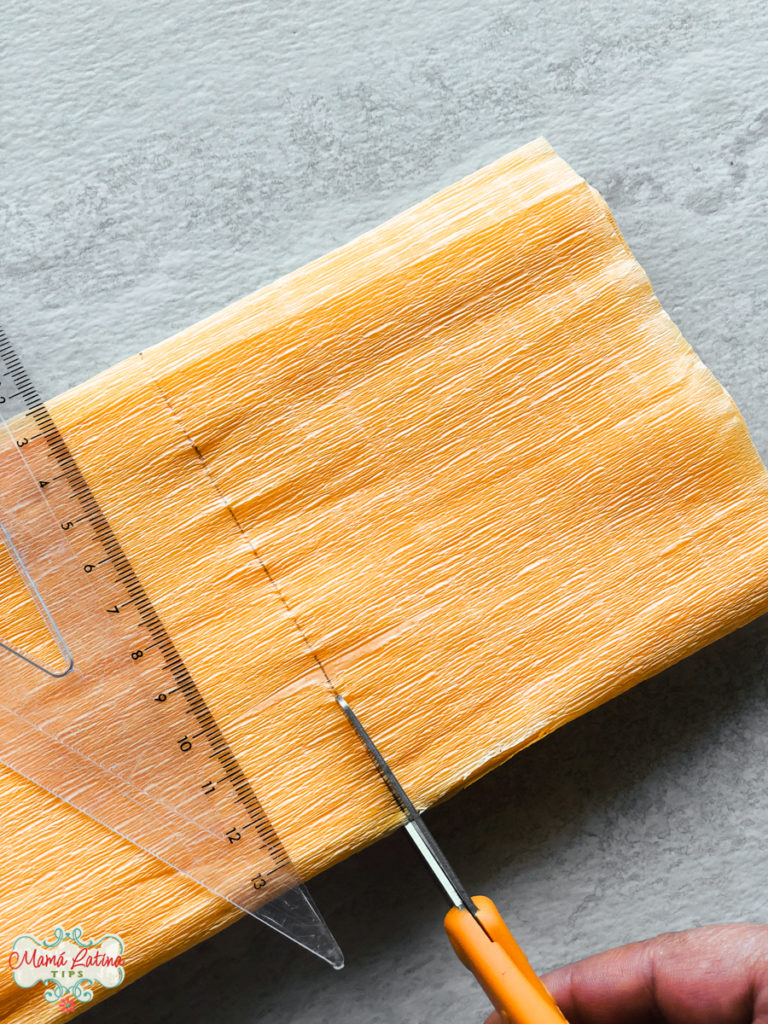 A person cutting a piece of crepe paper next to a ruler.