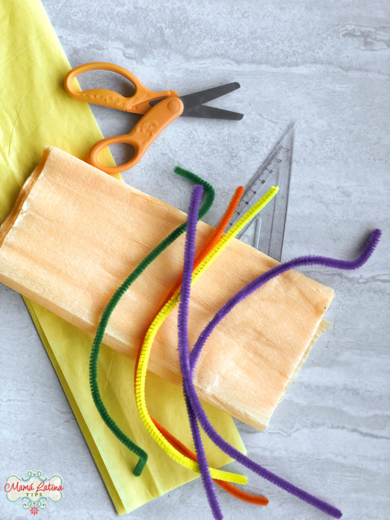 A pair of scissors, a ruler, pipe cleaners and a piece of paper on a table.