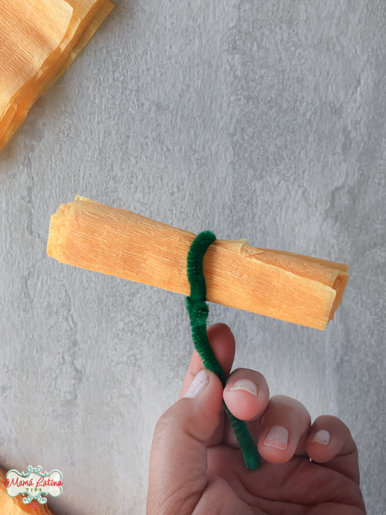 A person holding a strip of folded crepe paper with a green pipe cleaner attached to it.