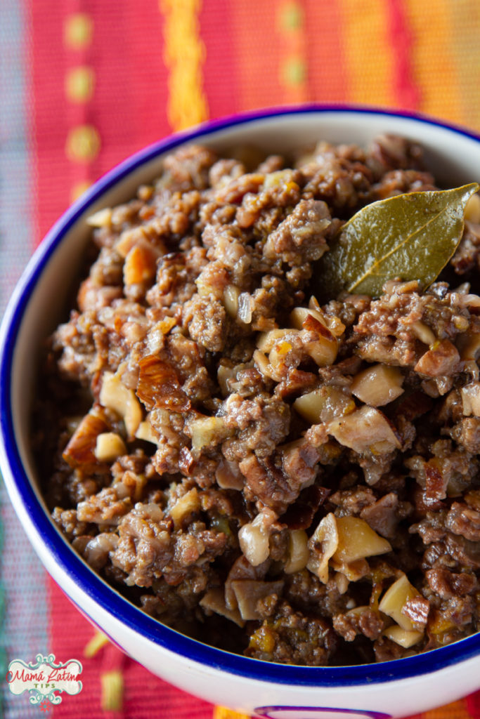 Un tazón con picadillo hecho don nueces, frutas y carne y una hoja de laurel