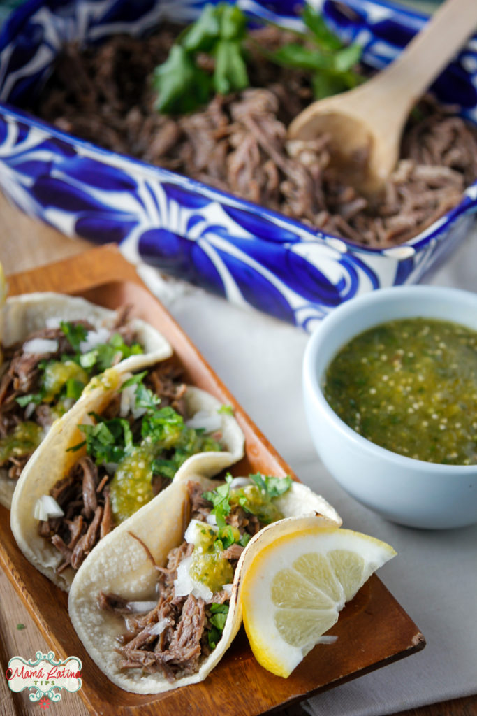 Tacos de barbacoa de res con salsa verde sobre un platón de madera