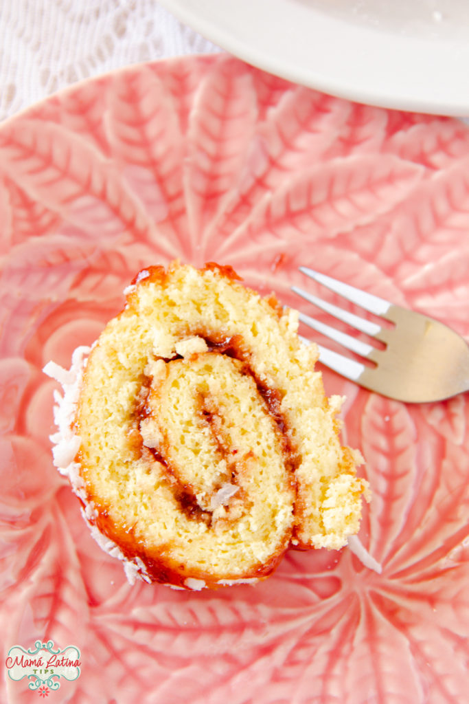 A slice of Mexican jelly roll with marmalade and coconut on a pink dish.