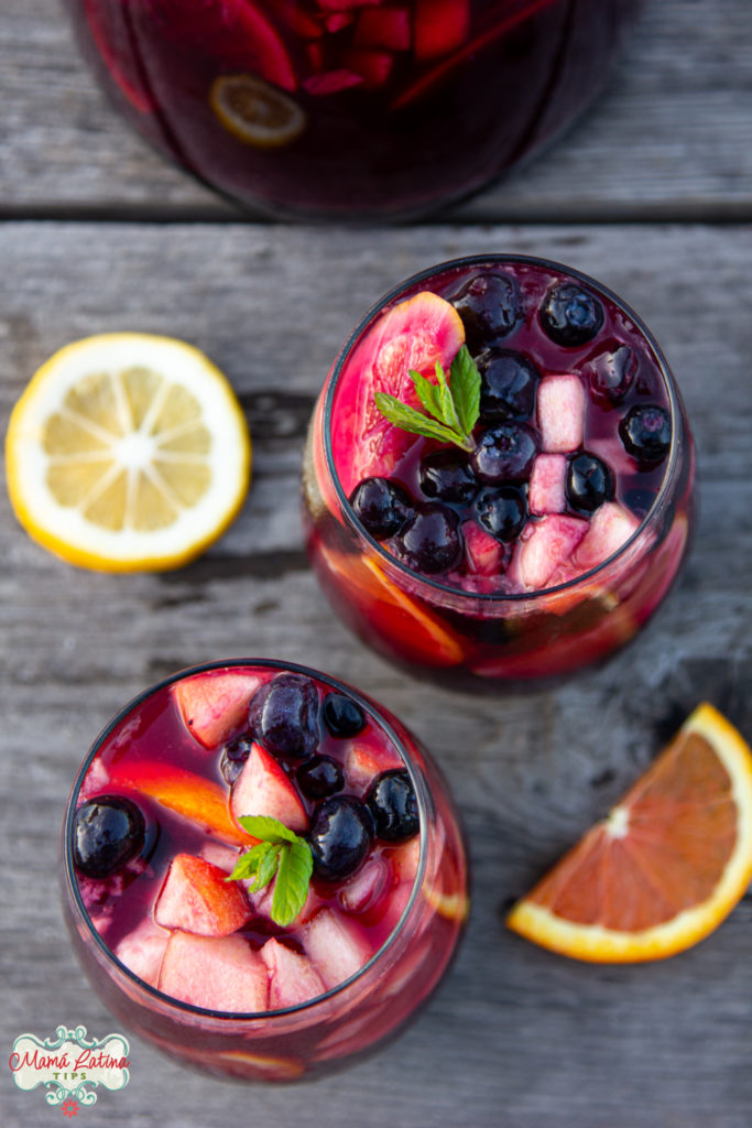 two glasses with sangría and fruit on a wooden table