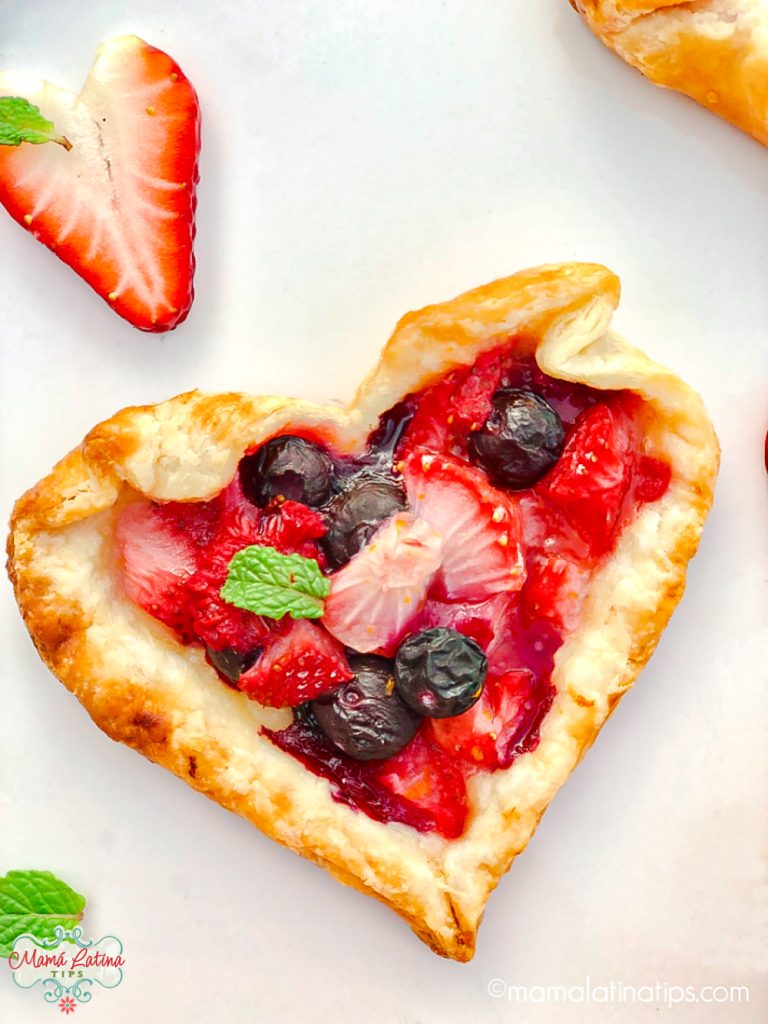 Una tarta en forma de corazón rellena de frutas rojas y adornada con una hoja de menta.