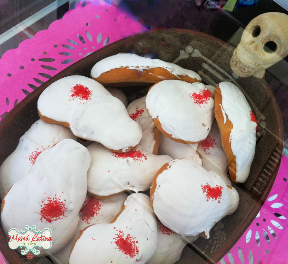 A display of pan de muerto ánimas on a table covered with pink papel picado.