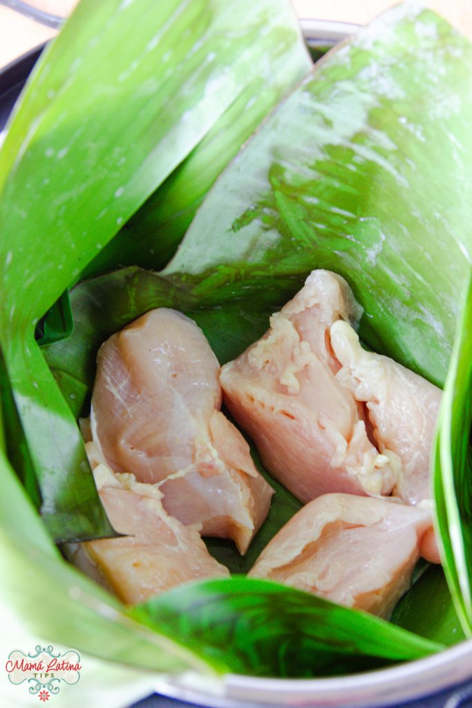 cinco pedazos de pollo crudo dentro de una olla cubierta de hojas de plátano
