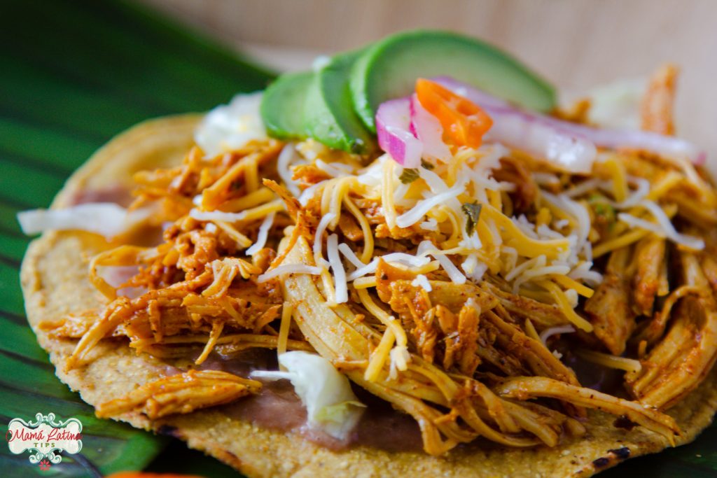 Una tostada con pollo pibil, queso y aguacate sobre una hoja de plátano