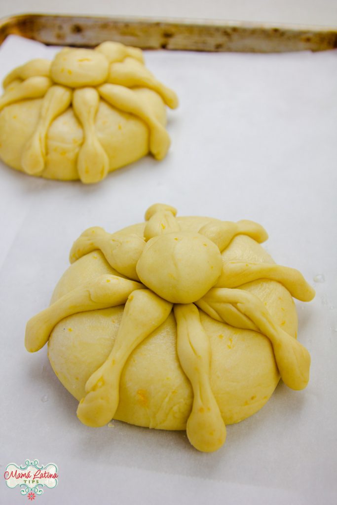 Two Day of the Dead bread loves on top of a parchment lined baking sheet, before baking. 