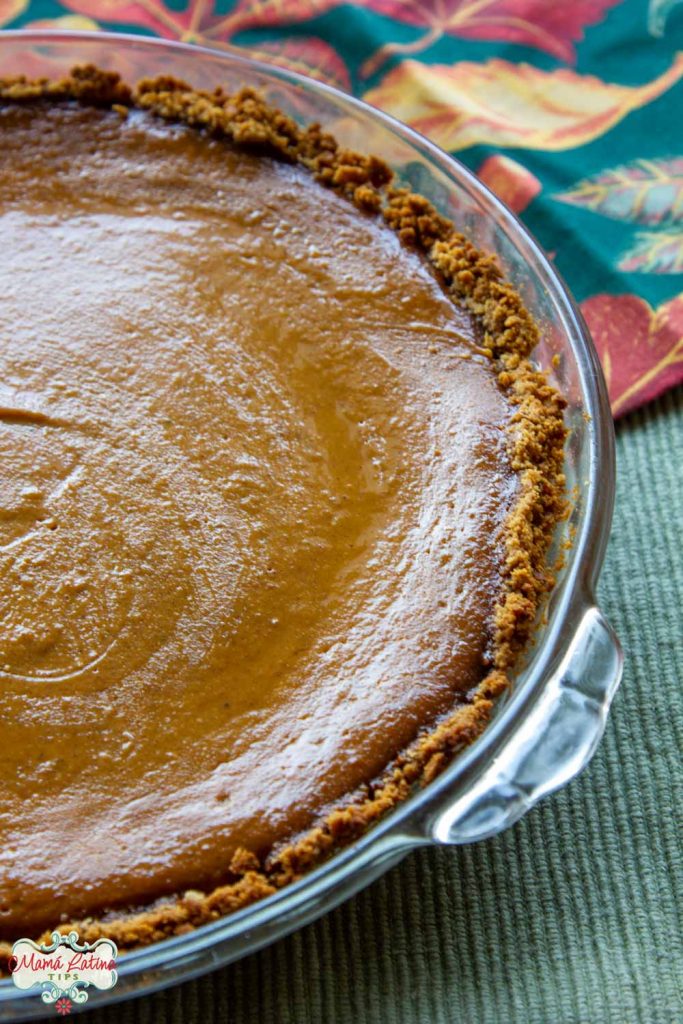 Pumpkin pie in a glass pan on top of a green tablecloth