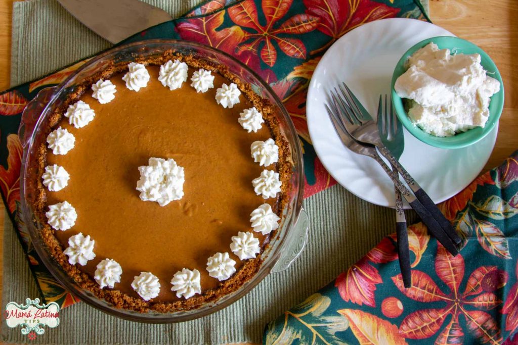 pumpkin pie with whipped cream rosettes next to a plate with forks and whipped cream