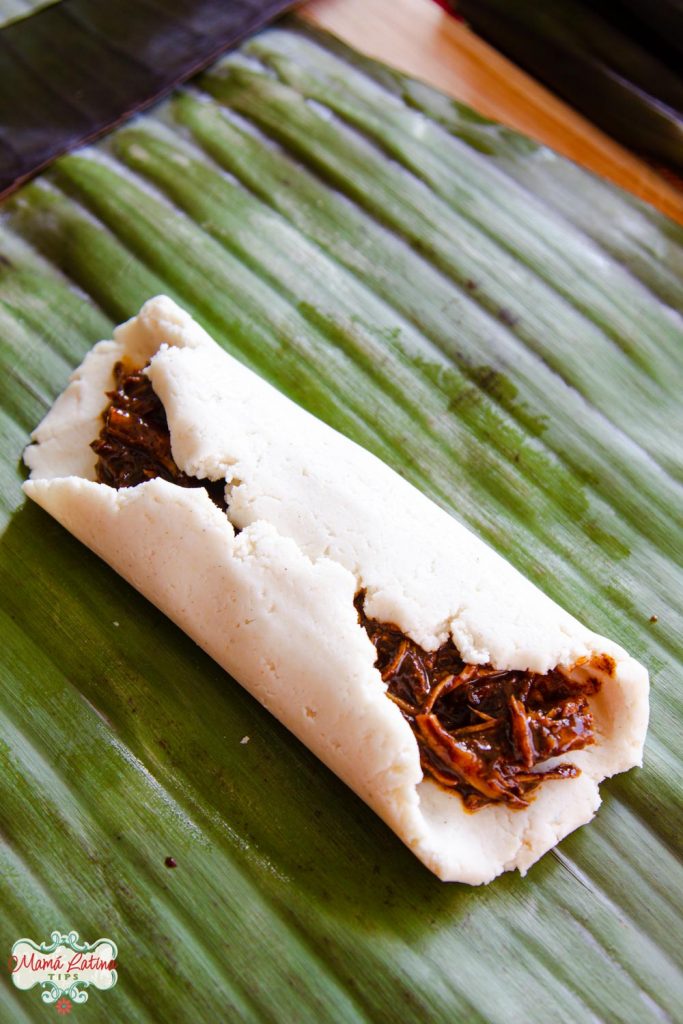 Tamal oaxaqueño relleno y crudo encima de una hoja de plátano