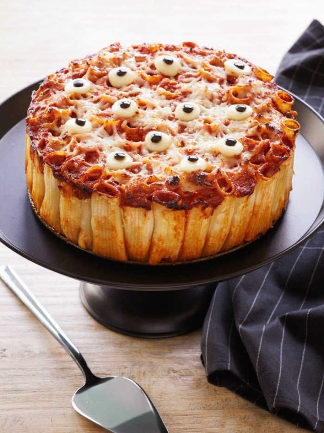 Un pay de pasta con salsa de tomate y ojitos de Halloween sobre un pedestal negro sobre una mesa de madera.