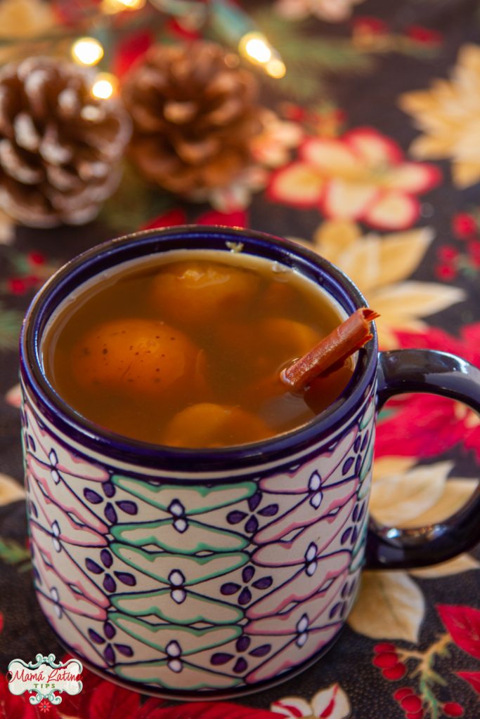 Una taza con ponche mexicano sobre un mantel de nochebuenas.