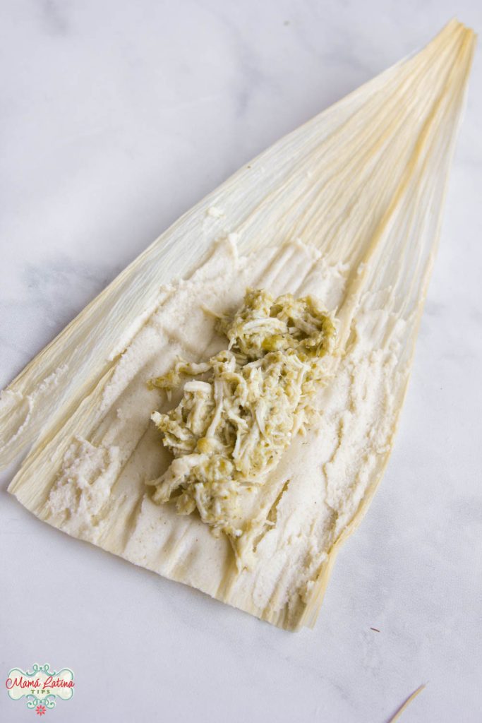 open corn husk with masa and chicken in green sauce