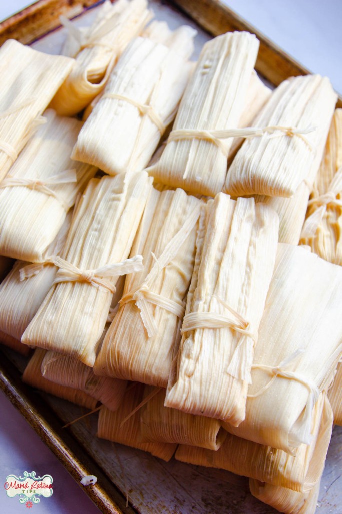 Mexican tamales wrapped in corn husks on a baking sheet.