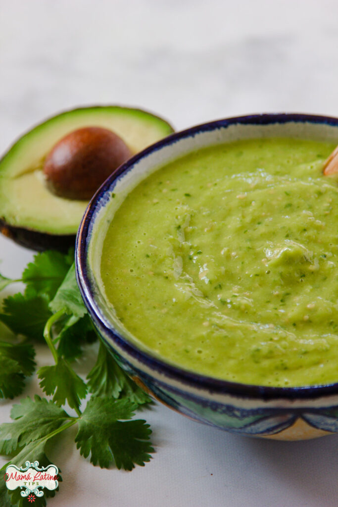 salsa de aguacate en una salsera de cerámica junto a cilantro fresco y medio aguacate