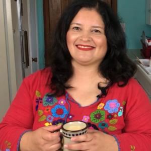 Silvia Martinez wearing a Mexican style red blouse and holding a ceramic cup