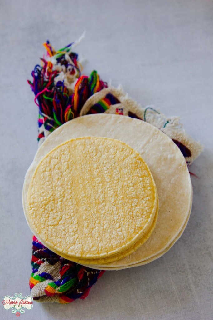 Two types of tortillas, regular size and taco size on top of a Mexican colorful napkin.