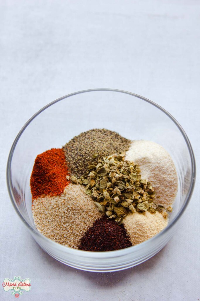 A small glass bowl with dry rub ingredients for a tri-tip roast, including, oregano, black pepper, paprika pepper, and garlic powder