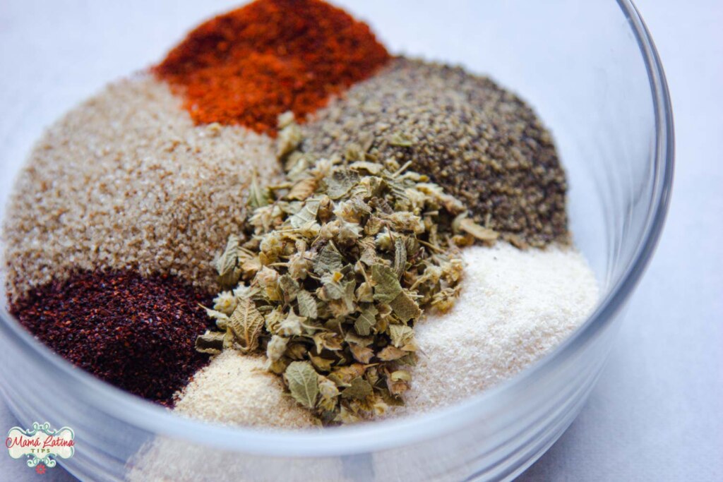 Mexican rub spices, including, dry oregano, cayenne pepper, blac pepper, chile ancho, garlic salt, garlic powder and onion powder in a glass bowl. 