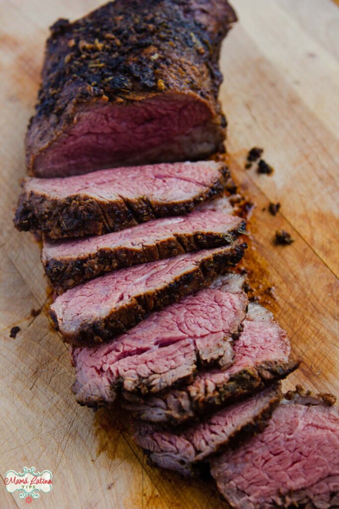 A sliced medium rare tri-tip roast on top of a wooden cutboard. 