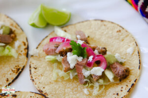 tri tip tacos with red onions, cheese and salsa with a couple of lime slices at the side.