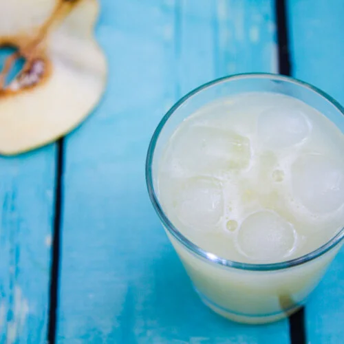 quince agua fresca in a glass next to a slice of quince on a blue wooden table