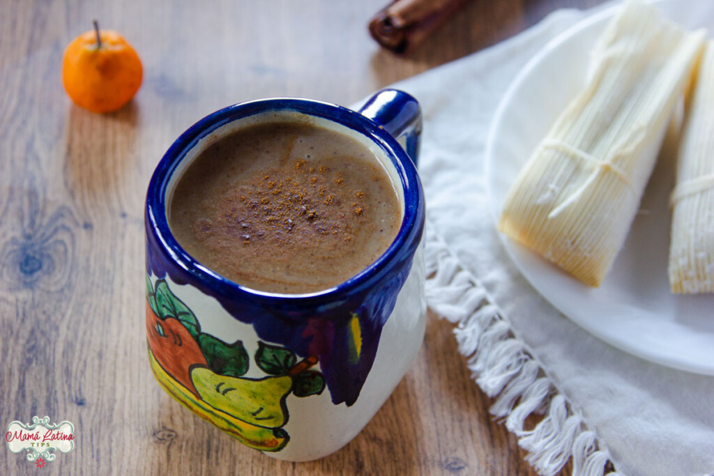 Ponche fruit atole in a Mexican ceramic cup with blue cobalt details next to a plate with tamales.