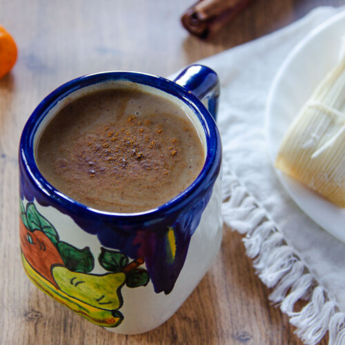 Ponche fruit atole in a Mexican ceramic cup with blue cobalt details next to a plate with tamales.