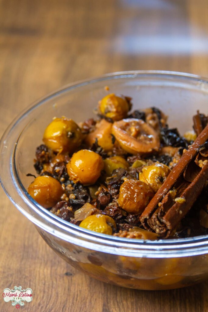 A glass bowl with Mexican Ponche fruit and a couple of cinnamon sticks on top of a wooden table.